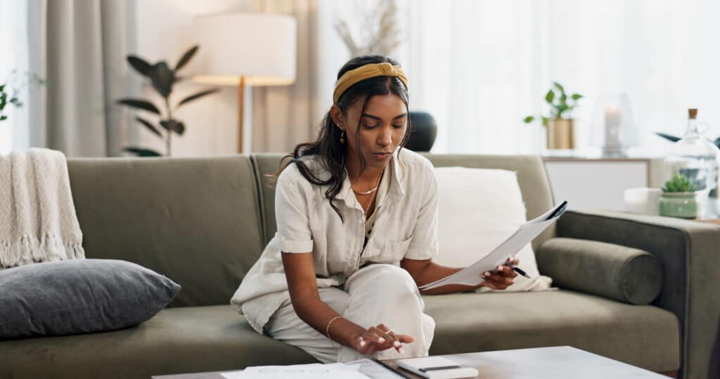 Woman reviewing tax documents on the sofa, trying to understand delinquent international information return submission procedures.