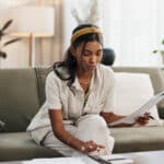 Woman reviewing tax documents on the sofa, trying to understand delinquent international information return submission procedures.