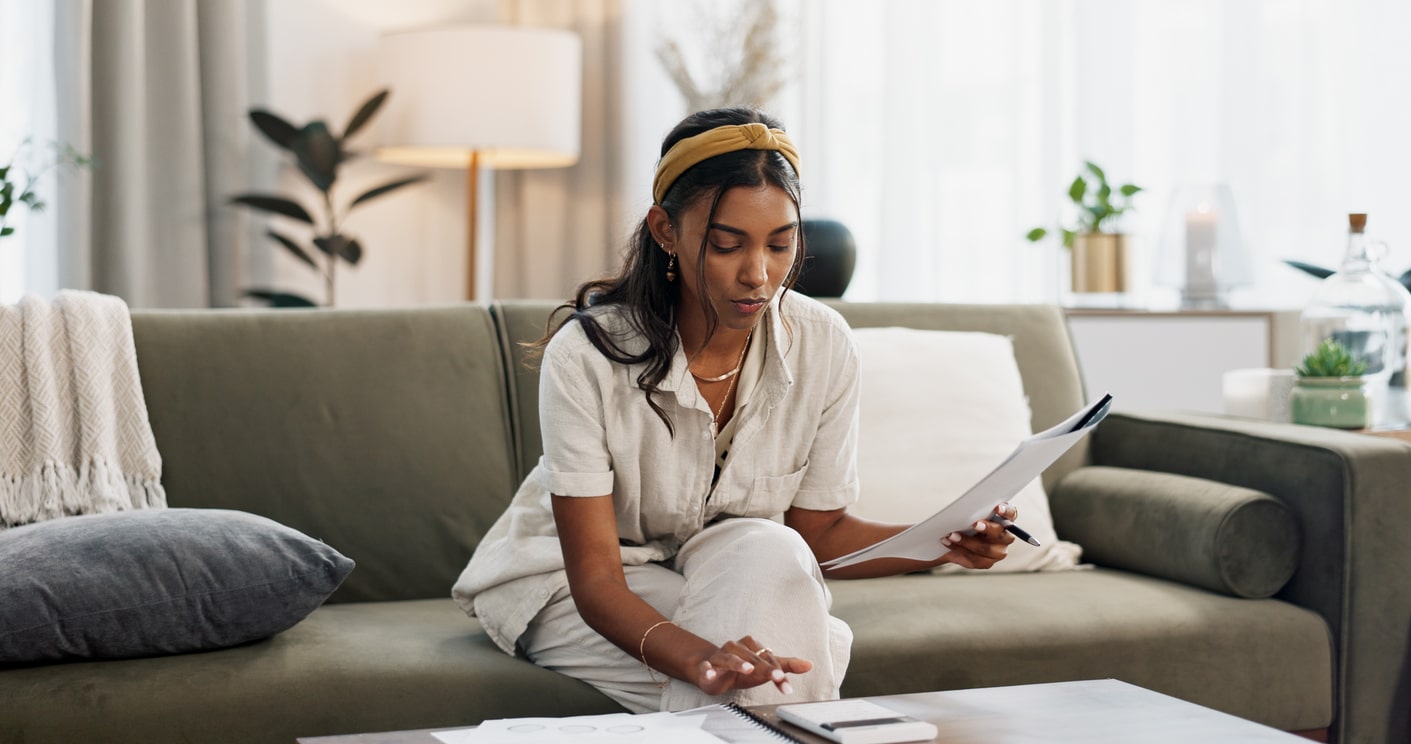 Woman reviewing tax documents on the sofa, trying to understand delinquent international information return submission procedures.
