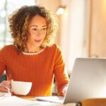 A woman sitting in front of her laptop with a cup of coffee