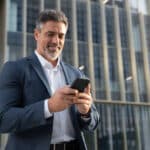 Confident businessman checks financial data on his phone, managing international income that may require Form 1118.