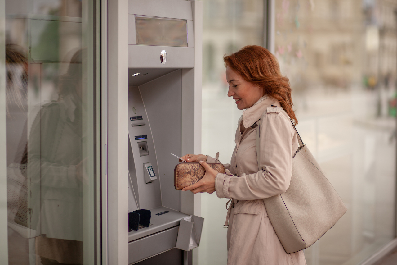 Mature woman using an ATM and putting her credit card away, reflecting everyday financial activity impacted by FATCA.