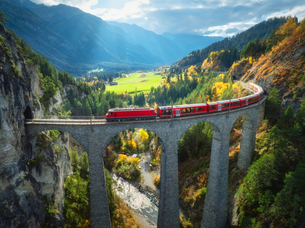 Red train crossing an alpine viaduct at sunset, capturing the dramatic landscapes surrounding Americans living in Switzerland.