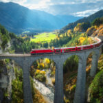 Red train crossing an alpine viaduct at sunset, capturing the dramatic landscapes surrounding Americans living in Switzerland.