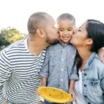 US parents kiss their child while spending time outside together.