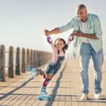 Father holding his child’s hands while she learns to roller skate on a beach promenade, a warm moment that reflects how the child tax credit supports everyday family life.