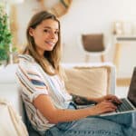 Smiling woman working from home, tracking travel days and eligibility for the physical presence test.