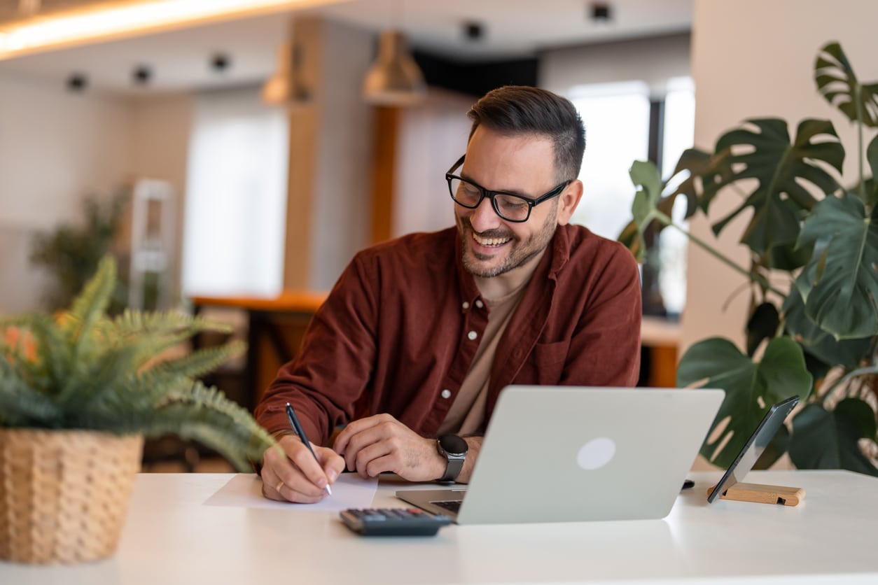 Young businessman working on a laptop and writing notes, planning around international payroll issues like a totalization agreement.