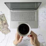 Freelancer counting U.S. dollars beside a laptop and charts, reflecting the currency conversions often needed when using IRS exchange rates.