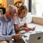 Senior couple reviewing finances with a calculator and laptop, reflecting the kind of foreign account reporting that may require FinCEN Form 114.