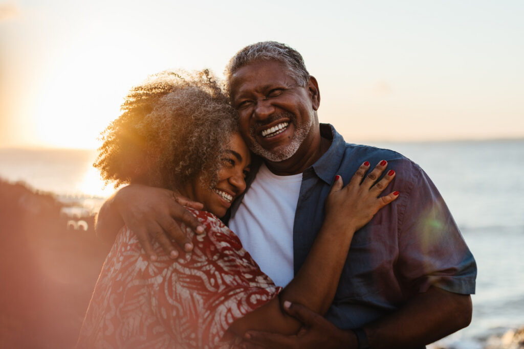 Older couple embracing by the sea at sunset, reflecting the lifestyle many imagine when they retire outside the US.