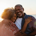 Older couple embracing by the sea at sunset, reflecting the lifestyle many imagine when they retire outside the US.