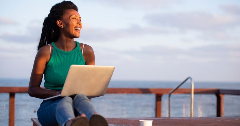 How to become a digital nomad in Bali - woman sitting on a dock with her laptop smiling, overlooking the ocean