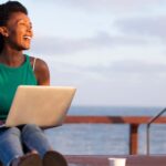 How to become a digital nomad in Bali - woman sitting on a dock with her laptop smiling, overlooking the ocean