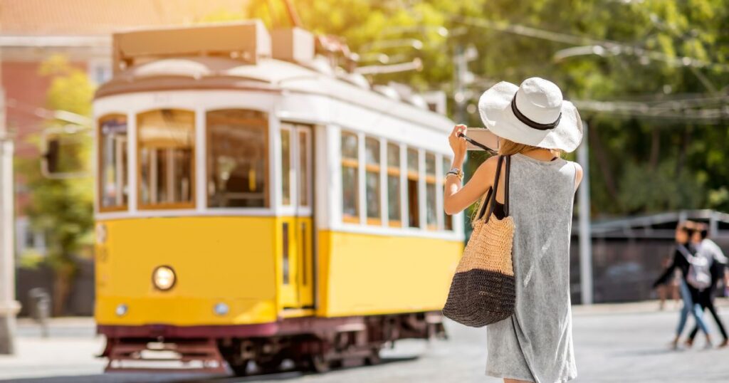 Tourist in Lisbon photographing classic yellow tram. Tourists do not have to pay tax in Portugal, but US expats who retire in Portugal do.