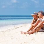 Retire in Mexico - older couple sitting on a beach looking at the water