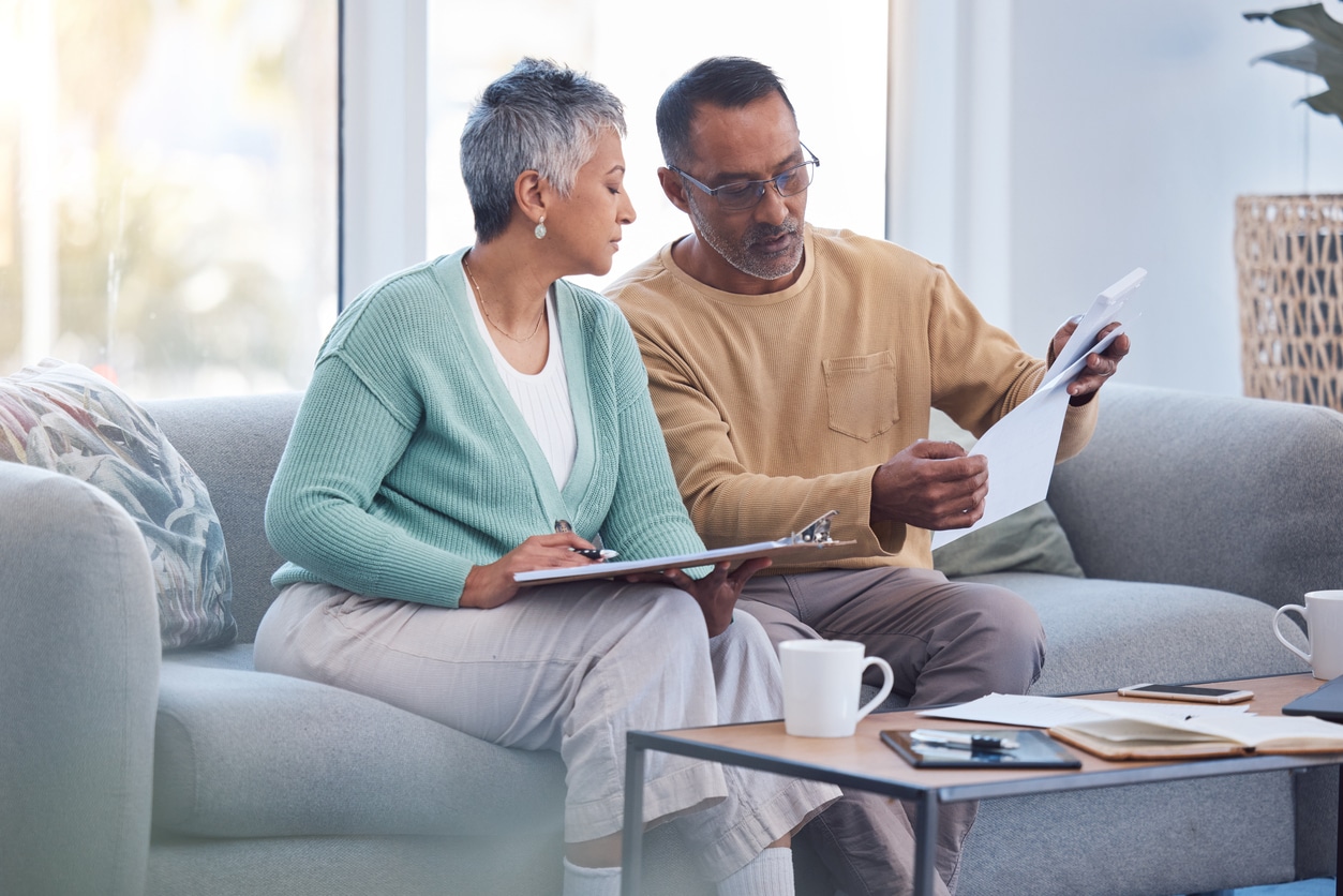 Senior couple sitting on the sofa reviewing bills and financial documents, illustrating how the windfall elimination provision can affect retirement planning decisions.