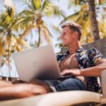 Best digital nomad jobs - man sitting under palm trees on a sunny day by the pool