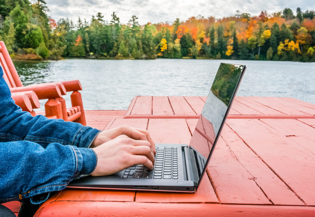 Digital nomad with a laptop near a tranquil lake in autumn, enjoying the freedom offered by the Canada digital nomad visa.