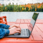 Digital nomad with a laptop near a tranquil lake in autumn, enjoying the freedom offered by the Canada digital nomad visa.