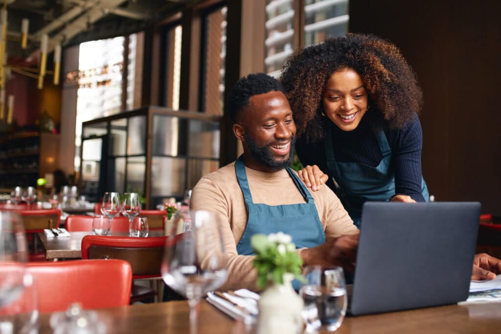 Small business owners using a laptop in a restaurant, reviewing income and adjustments that may be reported on IRS Schedule 1.