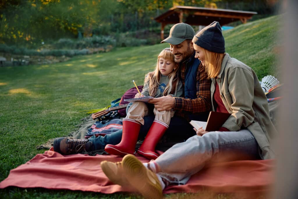 Parents and daughter relaxing outdoors with a notebook, representing the kind of everyday family finances affected by modified adjusted gross income.