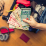 Female hands holding Asian currency and a foreign passport while preparing taxes as an expat.