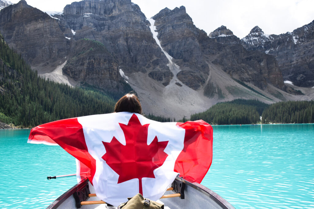 Young woman in a canoe holding a Canadian flag on Moraine Lake, symbolizing the adventure of Americans moving to Canada.