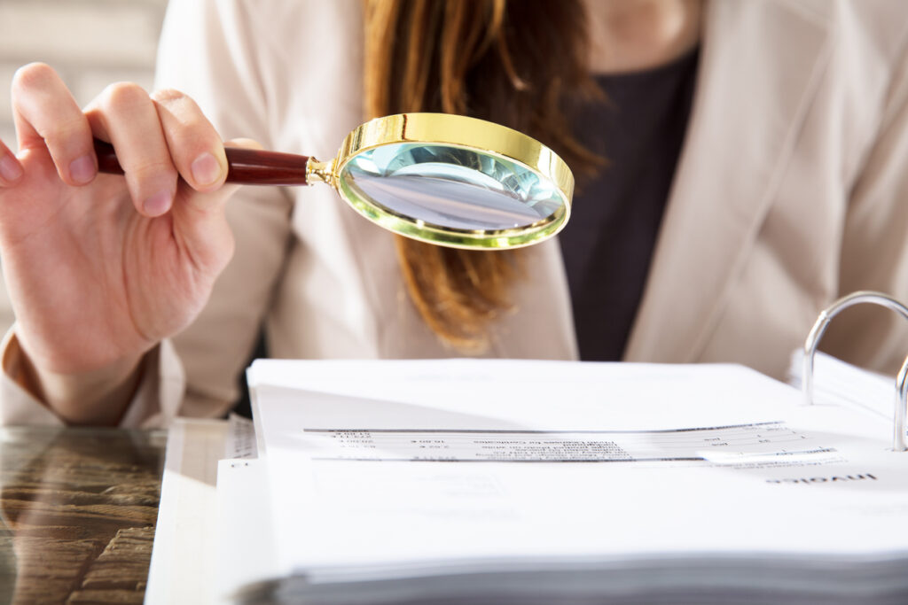 Close-up of a businesswoman using a magnifying glass to review financial documents, focusing on FATCA and CRS reporting requirements.