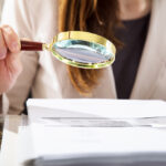 Close-up of a businesswoman using a magnifying glass to review financial documents, focusing on FATCA and CRS reporting requirements.