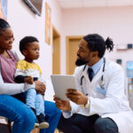 Smiling doctor speaking with a mother and son in a clinic—offering a glimpse into everyday healthcare in Canada.