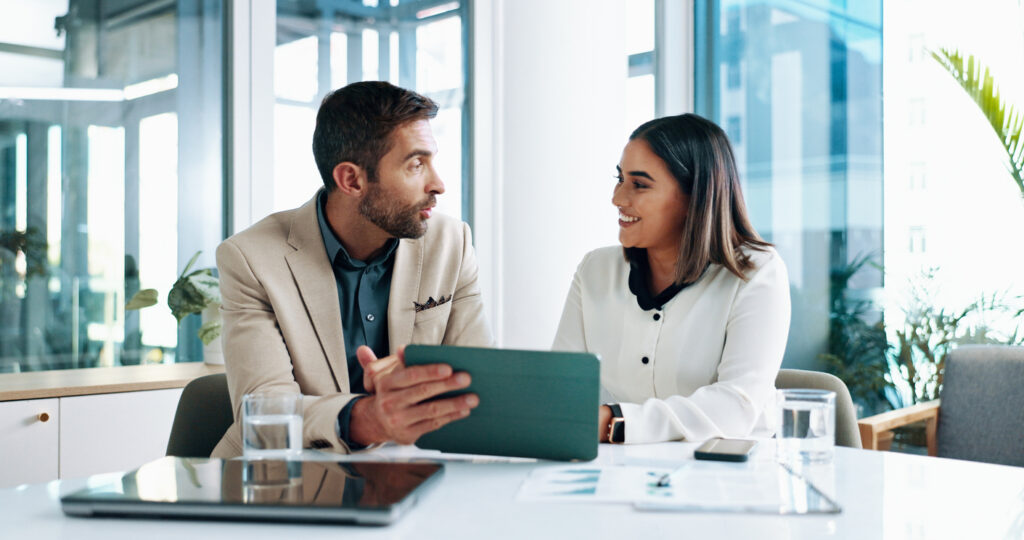 Smiling professionals reviewing financial data on a tablet—collaborating on business and wealth management UK strategies.