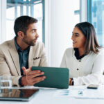 Smiling professionals reviewing financial data on a tablet—collaborating on business and wealth management UK strategies.