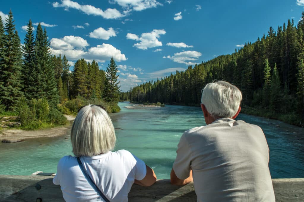 Older couple enjoying a quiet moment by the river, reflecting the peace of mind that comes with Canadian healthcare and retirement.