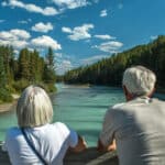 Older couple enjoying a quiet moment by the river, reflecting the peace of mind that comes with Canadian healthcare and retirement.