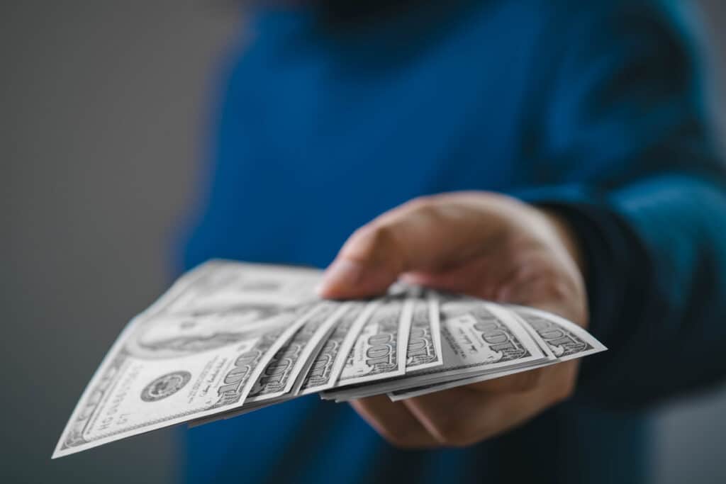 Hand offering U.S. dollar bills, symbolizing international payments and questions around remittance tax.