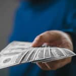 Hand offering U.S. dollar bills, symbolizing international payments and questions around remittance tax.