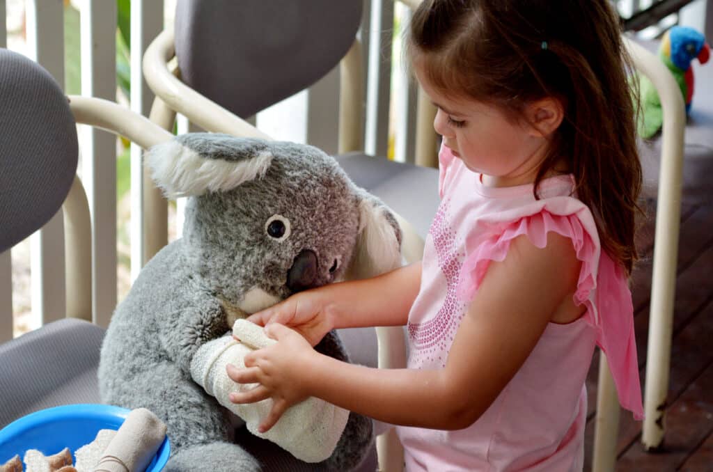 Little girl bandages a koala toy—playful look at healthcare in Australia.