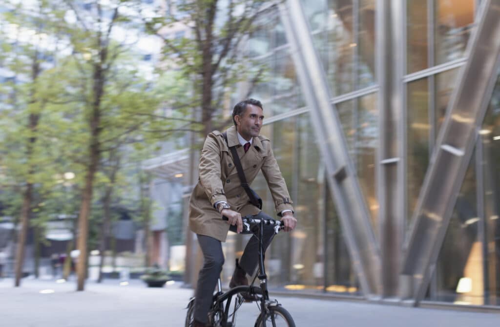 Businessman commuting by bike outside a sleek office building, symbolizing the professional lifestyle possible through a UK work visa for US citizens.