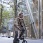 Businessman commuting by bike outside a sleek office building, symbolizing the professional lifestyle possible through a UK work visa for US citizens.