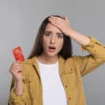Woman reacting with shock while holding a credit card, capturing the confusion around the question: is scammed money tax deductible.