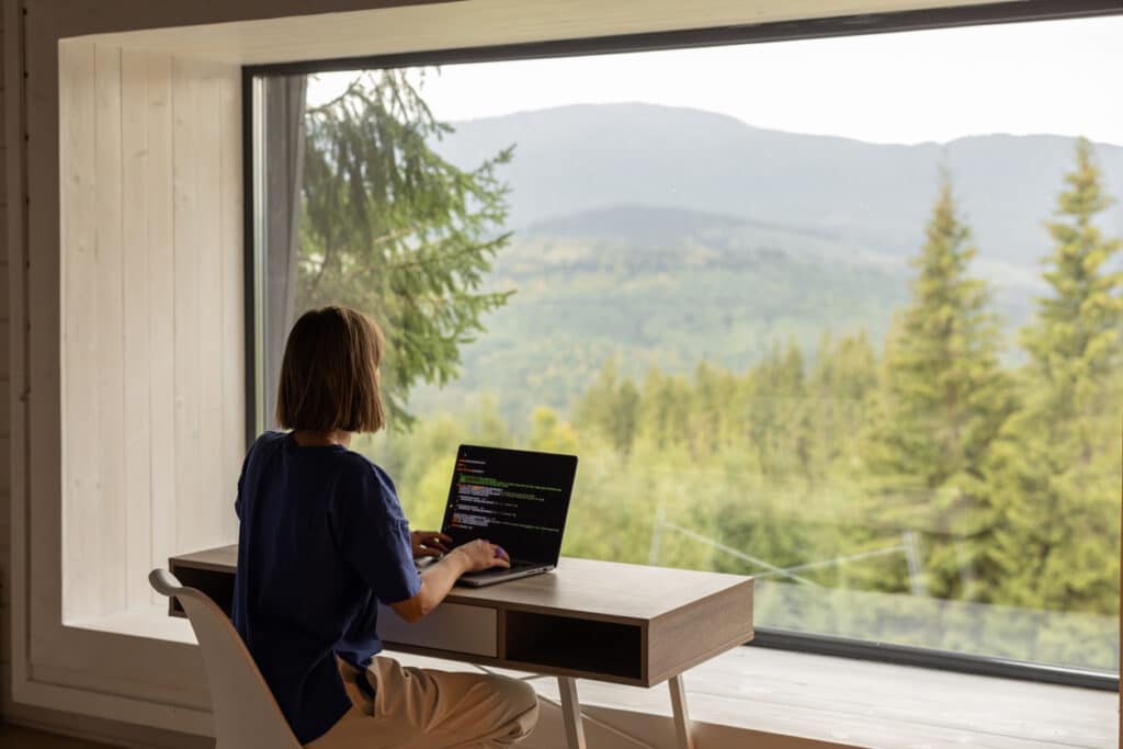 Woman working remotely with a mountain view, illustrating the lifestyle of someone working for an American company abroad.