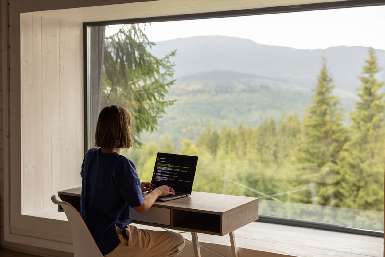 Woman working remotely with a mountain view, illustrating the lifestyle of someone working for an American company abroad.