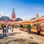 People shopping at outdoor market stalls in Mannheim, reflecting the everyday expenses behind the cost of living in Germany vs US.