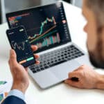 Hands holding a smartphone with a price chart, symbolizing cryptocurrency tax reporting.