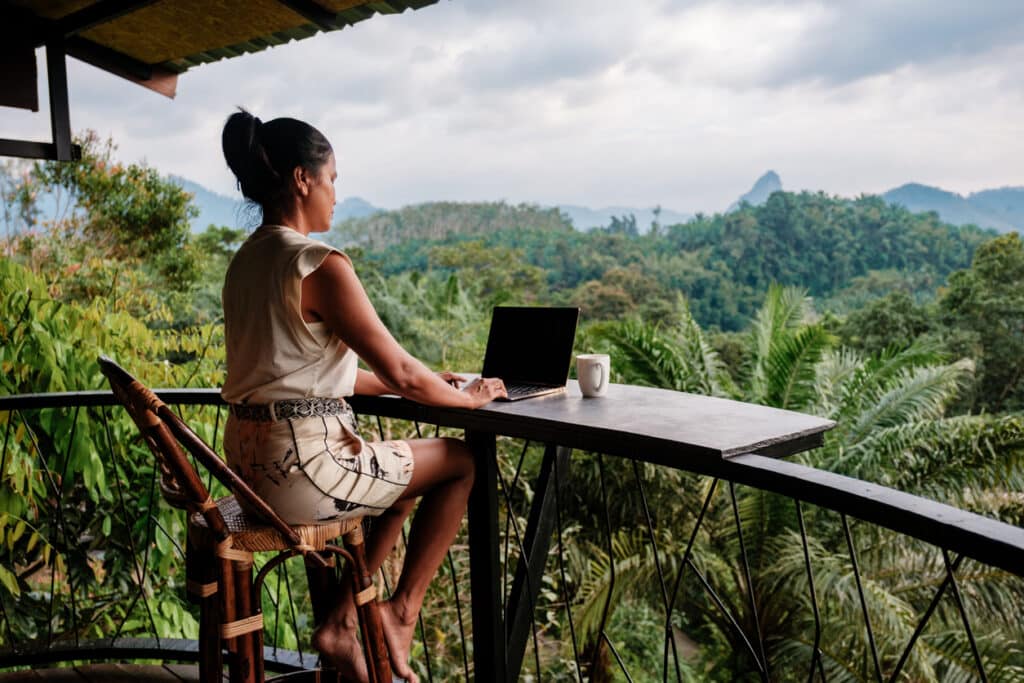 Woman working on a laptop in lush mountain scenery, capturing the freedom and calm of the digital nomad lifestyle.