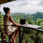 Woman working on a laptop in lush mountain scenery, capturing the freedom and calm of the digital nomad lifestyle.